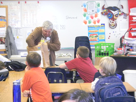 volunteer reaching into shopping bag as a classroom of youth watches