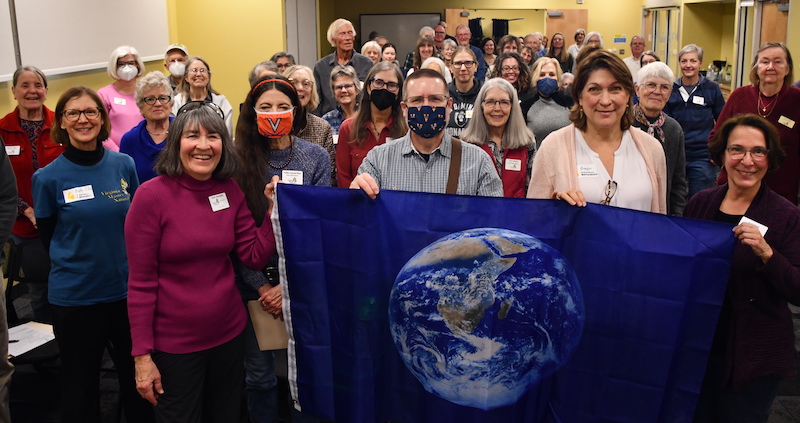 group of more than 30 people posed together, holding a blue flag with an image of Planet Earth