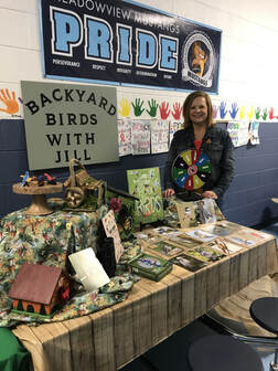 volunteer standing next to table with photos, books, and models for learning about birds
