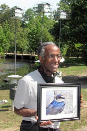 photo of a man in a park, holding a framed photo of a bird