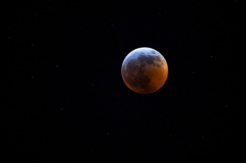 The moon, blue on top and blood red on the bottom in a black night sky dotted with stars