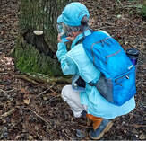 person with blue backpack crouched to take a photo of a mushroom