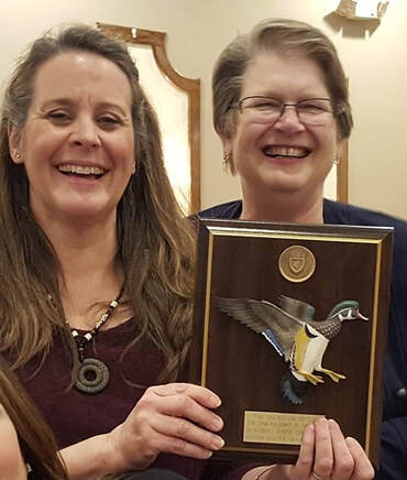 Two women holding an award plaque from Ducks Unlimited.