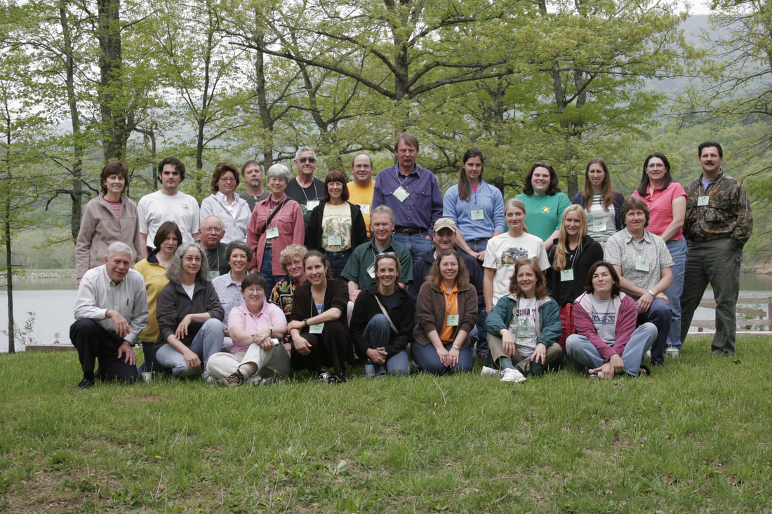 30+ people posed on a lawn next to a lake