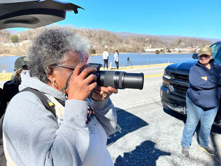 woman standing on a road by a lake pointing a camera