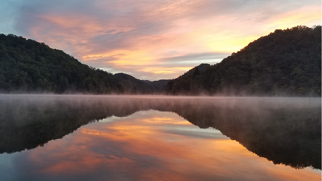 mist rising on a lake surrounded by forested hills