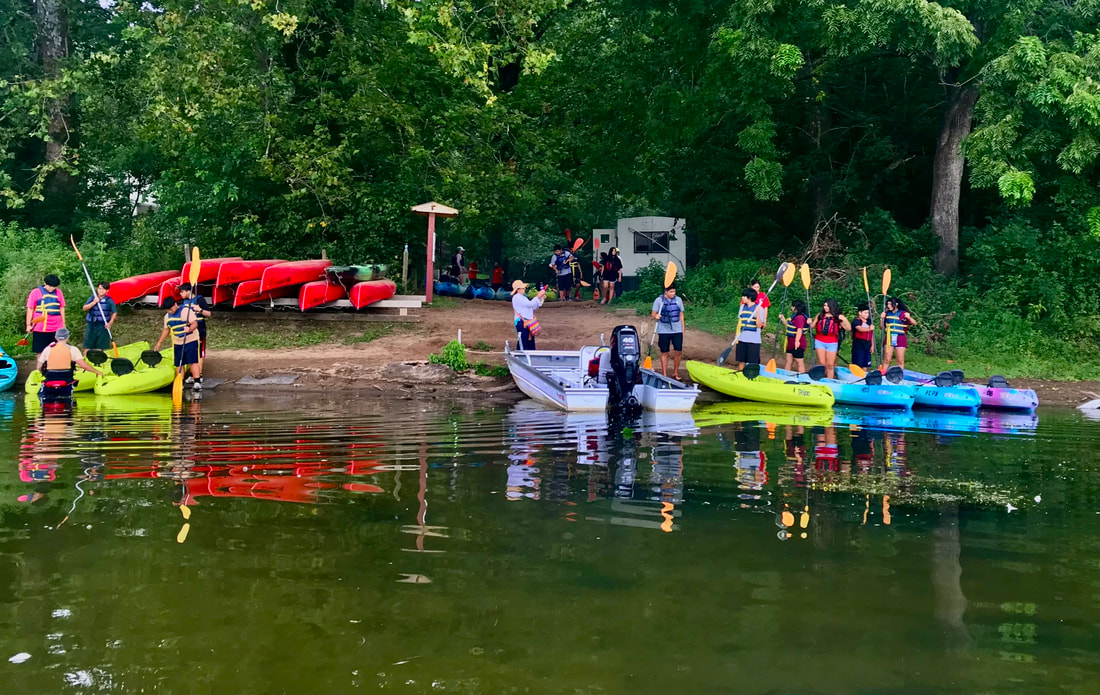 group of youth standing by kayaks at a lake