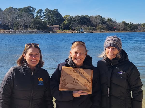 woman holding award plaque posed with two other people next to a large body of water