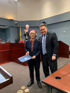 Woman holding certificate standing next to a man, person applauding in background
