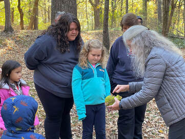 Person showing a large green fruit to a group of adults and children