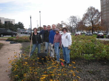 six volunteers posed in a garden with planting tools