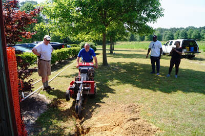 person using a machine to dig a trench while 3 other people watch